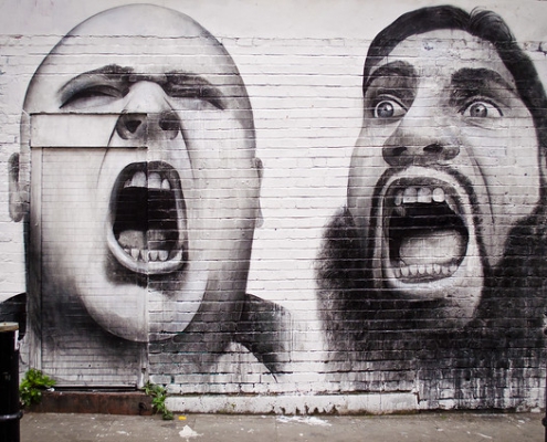 Une graffiti sur un mûr avec deux visages d'hommes de différentes ethnies et en colère.